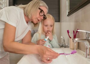 Photograph of woman showing child how to rinse toothbrush