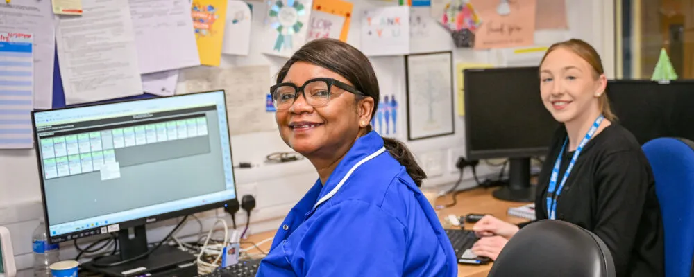 Two members of staff sat at a desk smiling at the camera